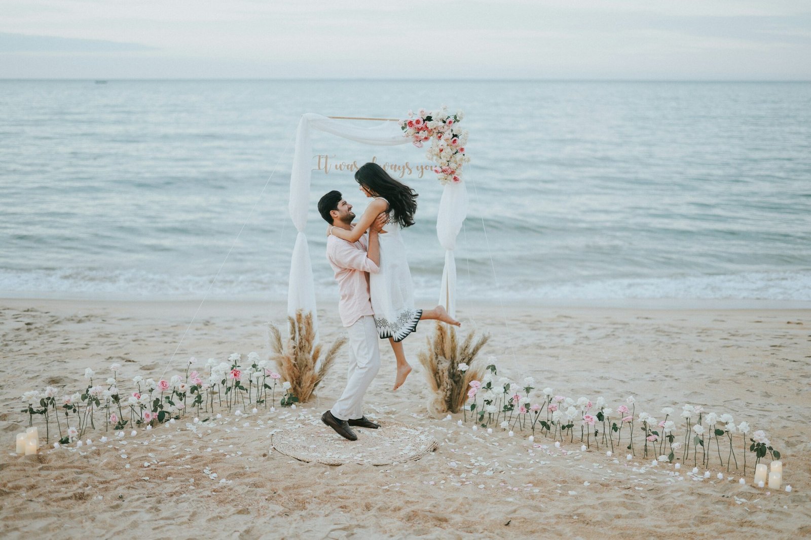 Couple celebrating beside a floral arch on a beach